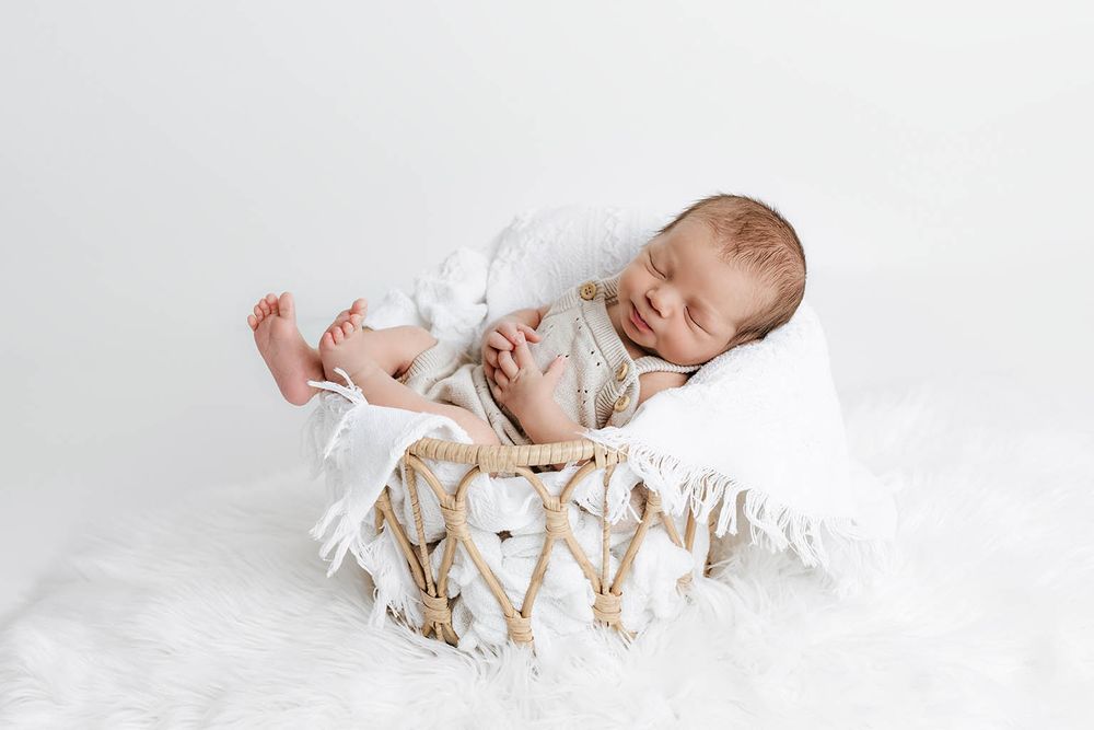 Newborn baby sleeping in a wicker basket with white blanket and fur rug in a studio setting by Romoland newborn photographer.