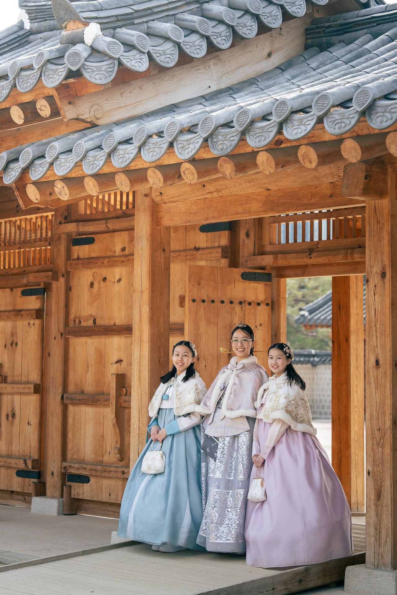 Three women in traditional Korean hanbok dresses pose at a wooden gate of a historic Korean palace.