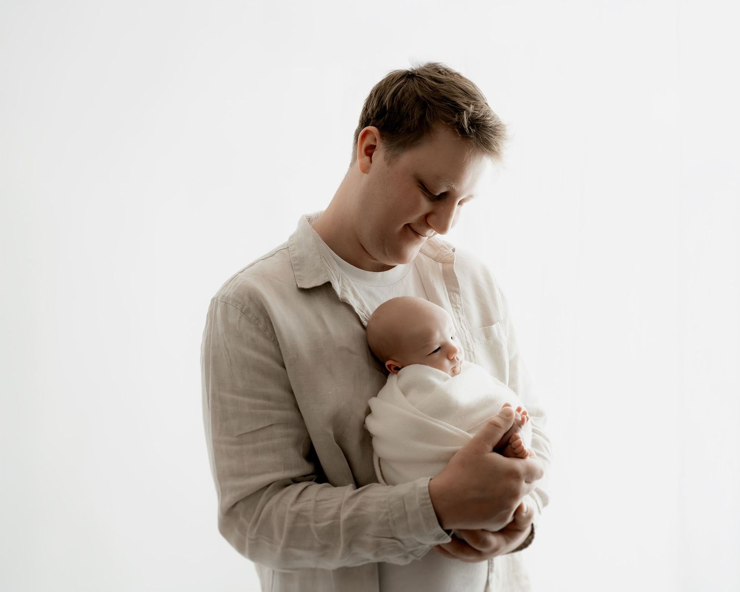 father holding newborn baby wrapped in natural fabrics during session in photography studio