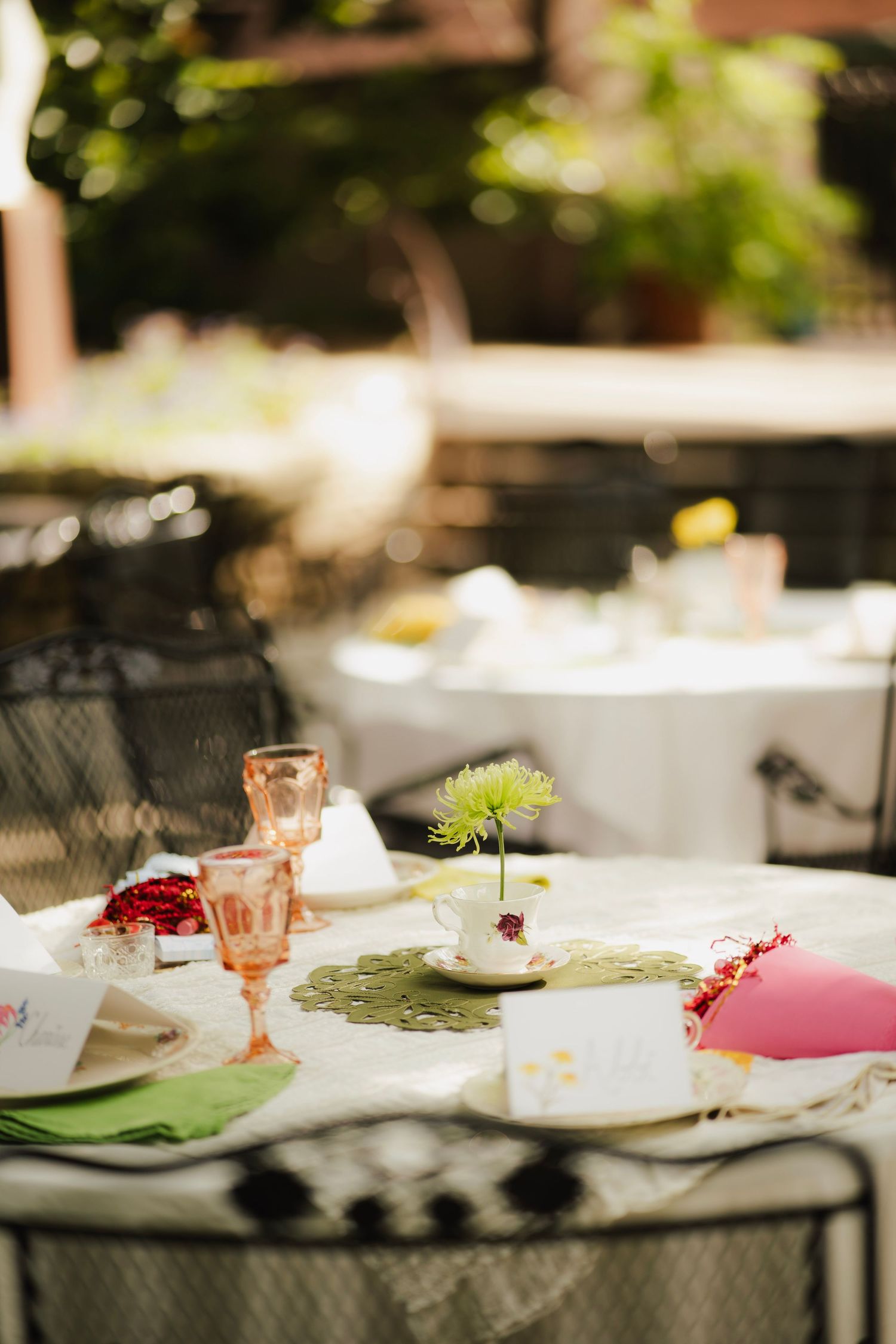 Elegant outdoor garden party table setting with pink glassware, green napkins, and floral centerpiece.