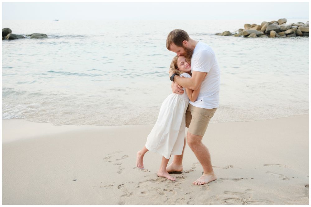 Couple dancing and embracing barefoot on a sandy beach with ocean waves nearby.