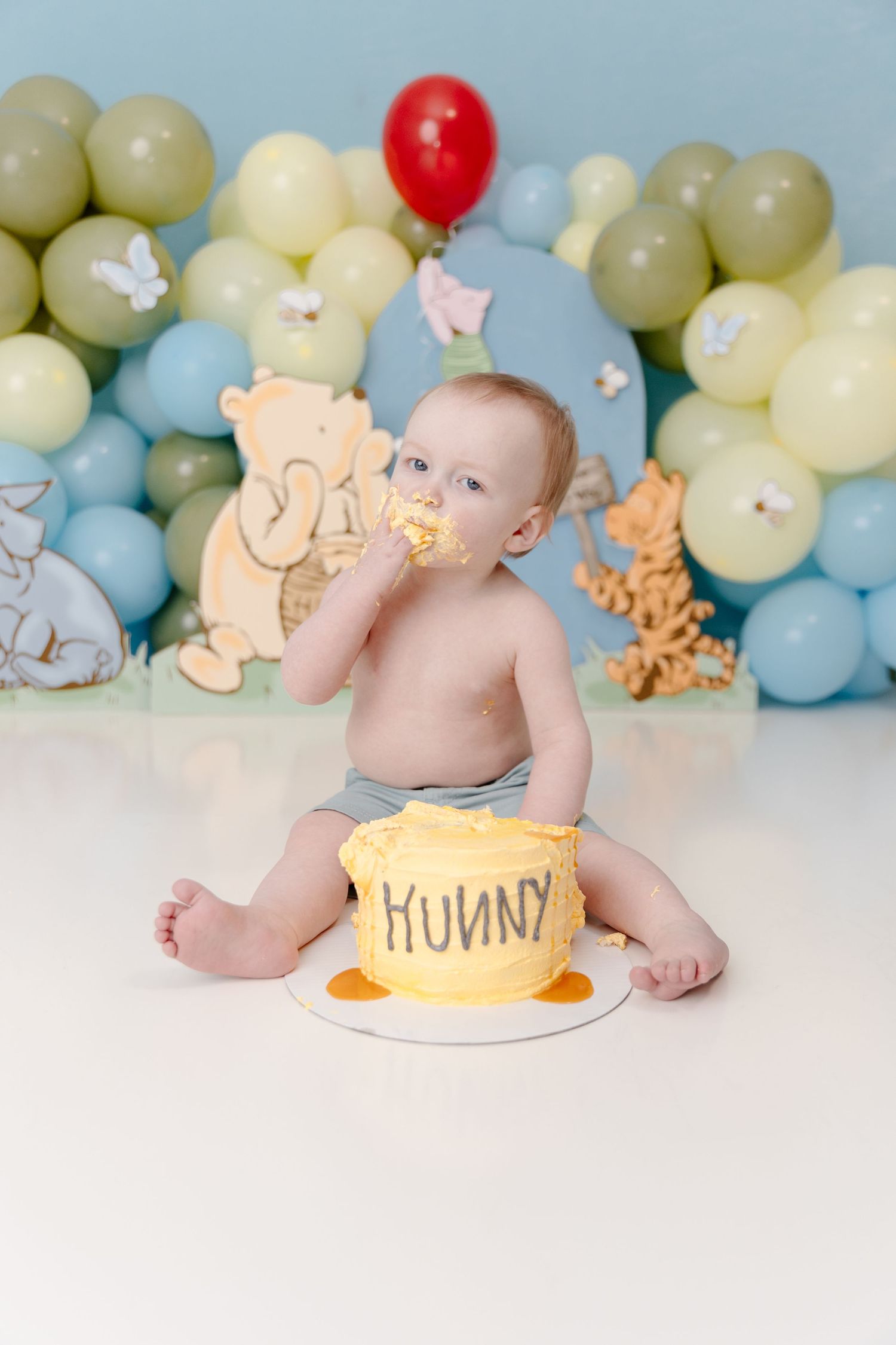 Baby smashing a yellow Hunny pot cake at a Winnie the Pooh first birthday party with balloon backdrop.