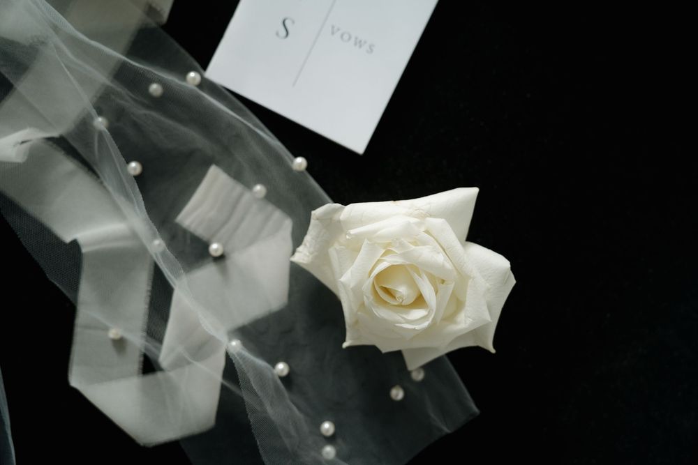 Elegant white rose boutonniere with pearl-adorned tulle veil displayed on dark background for wedding.