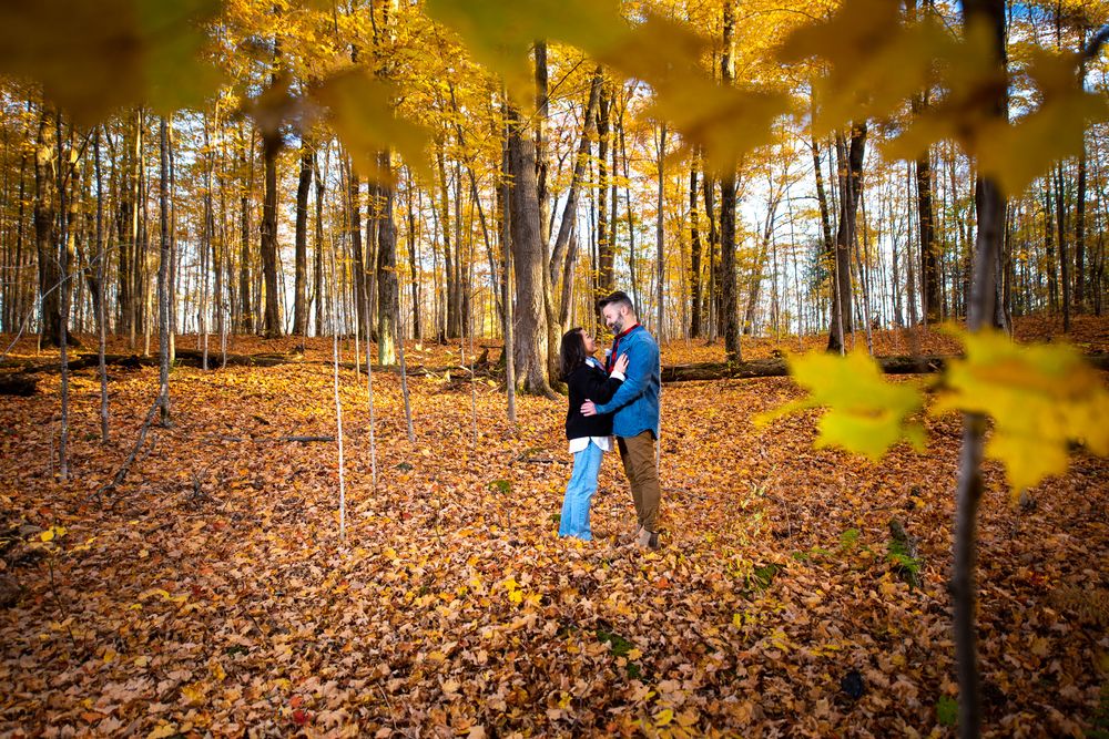 Couple embracing in a golden autumn forest framed by yellow leaves.