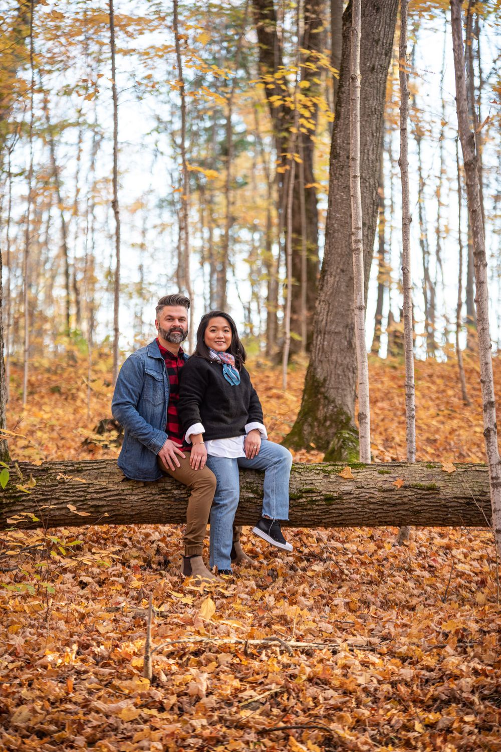Couple sitting on a fallen log in a colorful autumn forest.