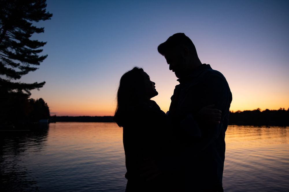 Romantic silhouette of a couple facing each other at sunset by a lake.