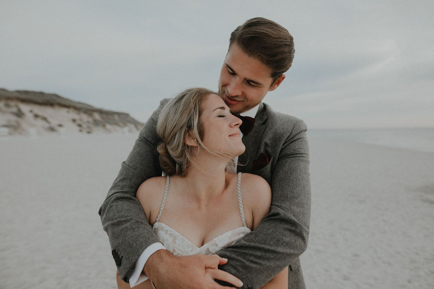 Romantic beachside wedding photos with couple sharing intimate moments against sandy backdrop.