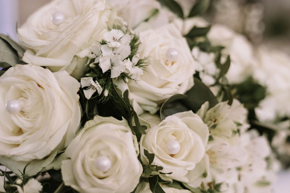 Nahaufnahme eines Brautstraußes mit weißen Rosen, Perlendekoration und feinen Blüten.