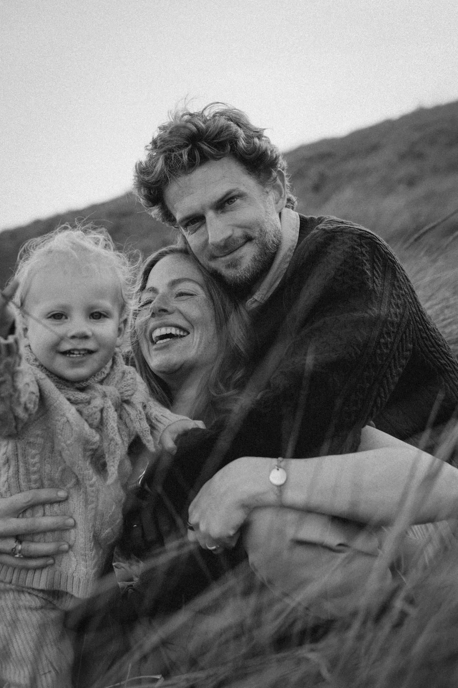 Black and white photo of a happy family with a young child smiling outdoors in a grassy field.