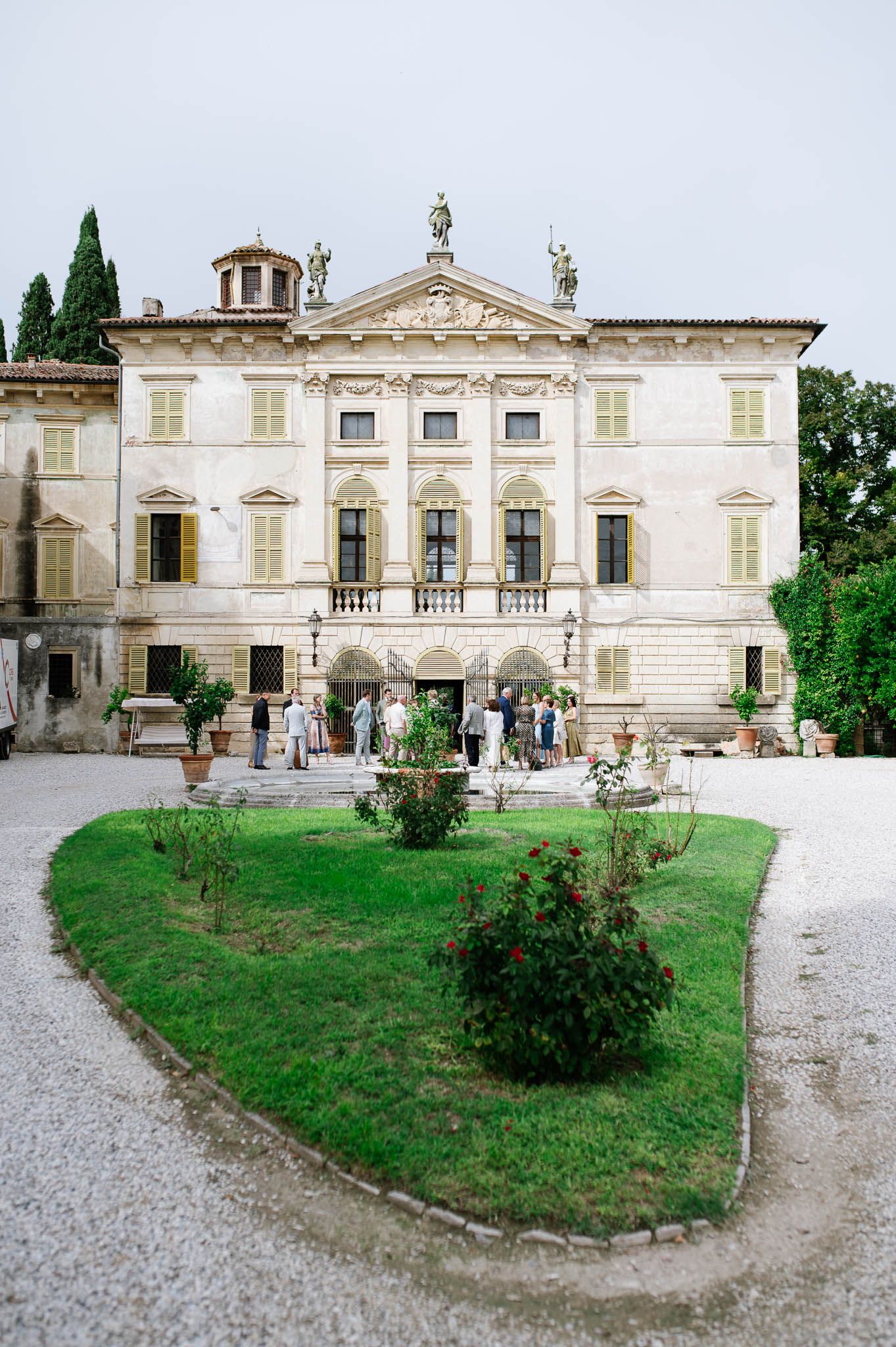 Elegant Italian villa with manicured gardens and guests gathering on the steps during a wedding celebration.