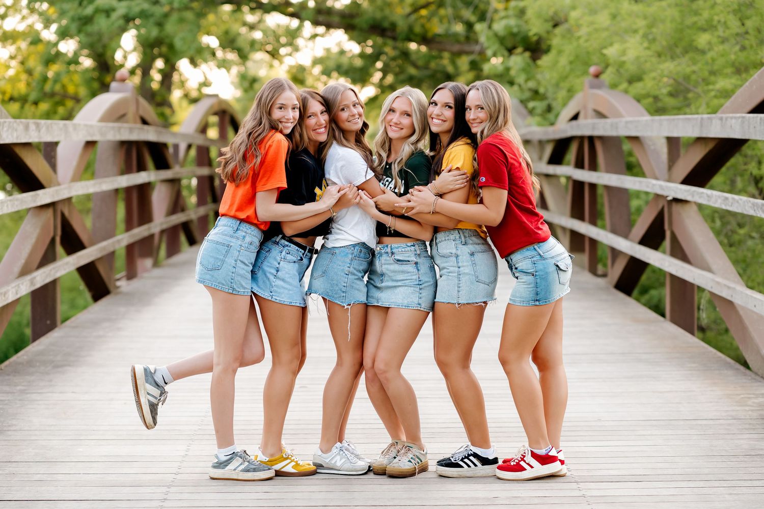 Group of seven young women posing together on wooden bridge for outdoor graduation photos.
