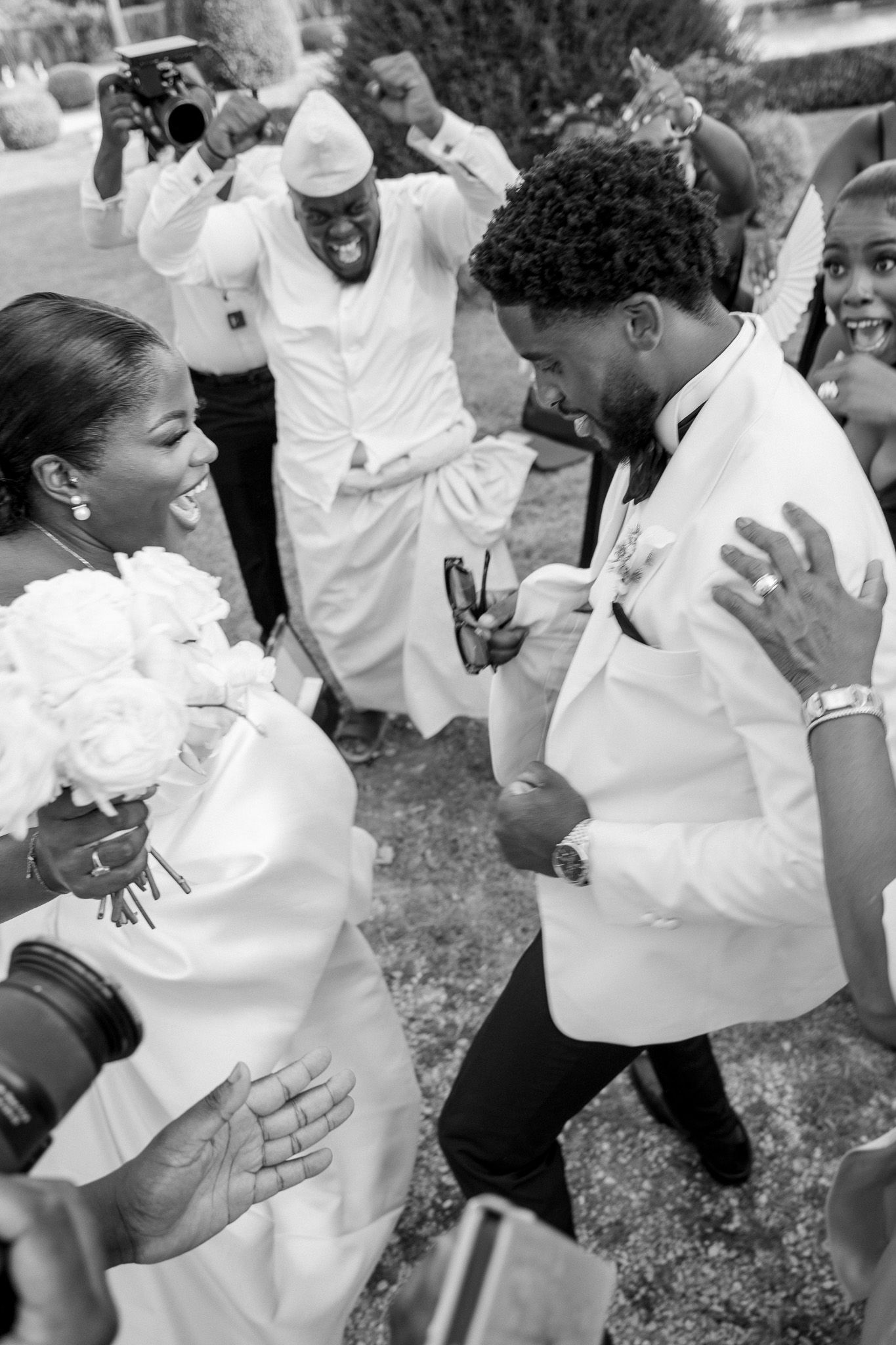 Black and white photo of a joyful bride and groom dancing at their wedding celebration outdoors.
