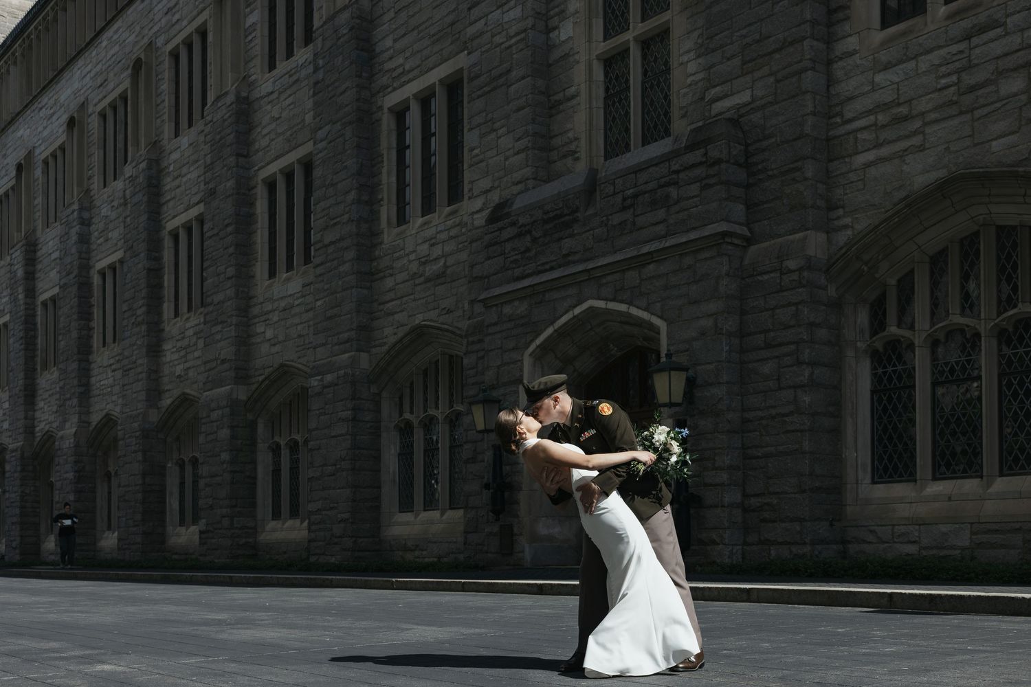 Bride and groom share a romantic dip kiss outside a historic stone building on their wedding day.