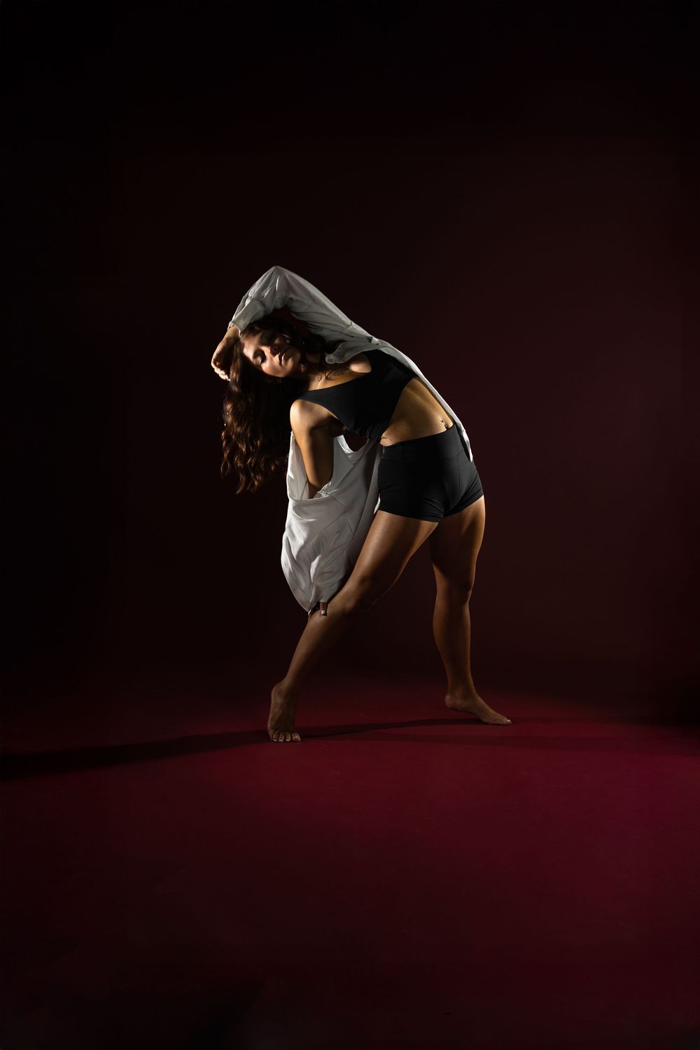 A contemporary dancer performs a dramatic movement sequence on a dark stage with dramatic lighting and shadows.