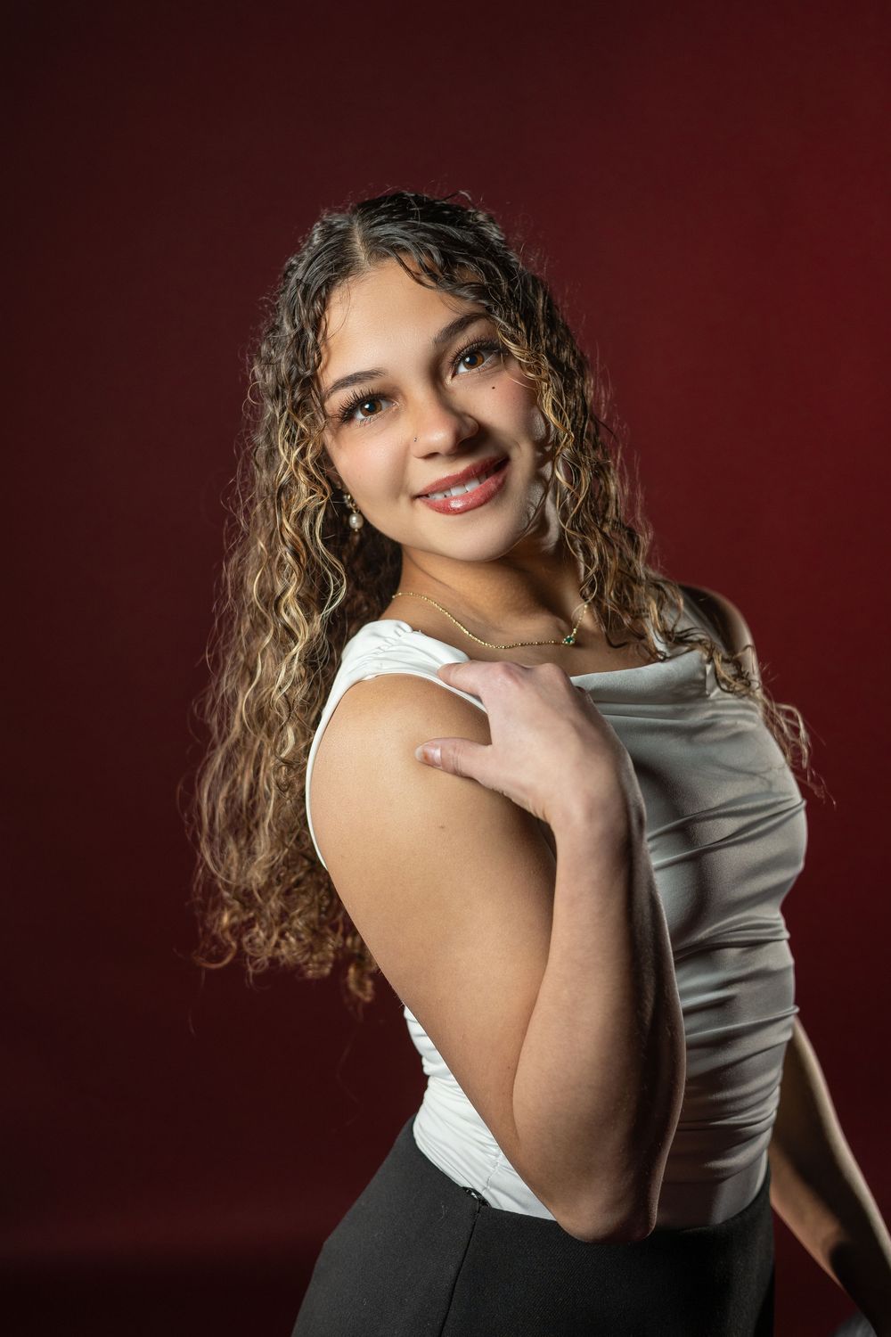 Portrait series showing a person with curly hair in a white and gray outfit posing against a dark red background.