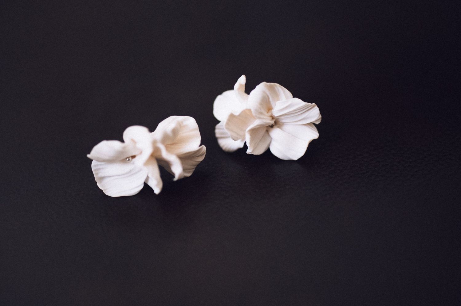 Two white ceramic flower earrings on a dark background.