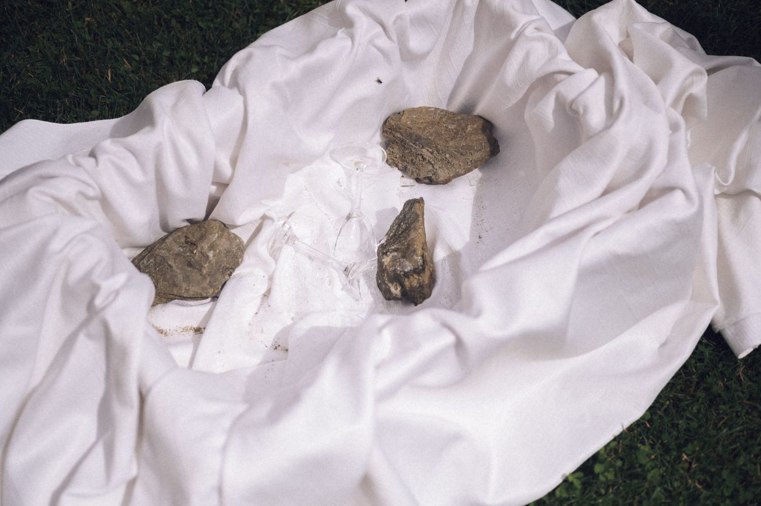 Rocks and wrapped artifacts displayed on a white cloth spread over green grass.