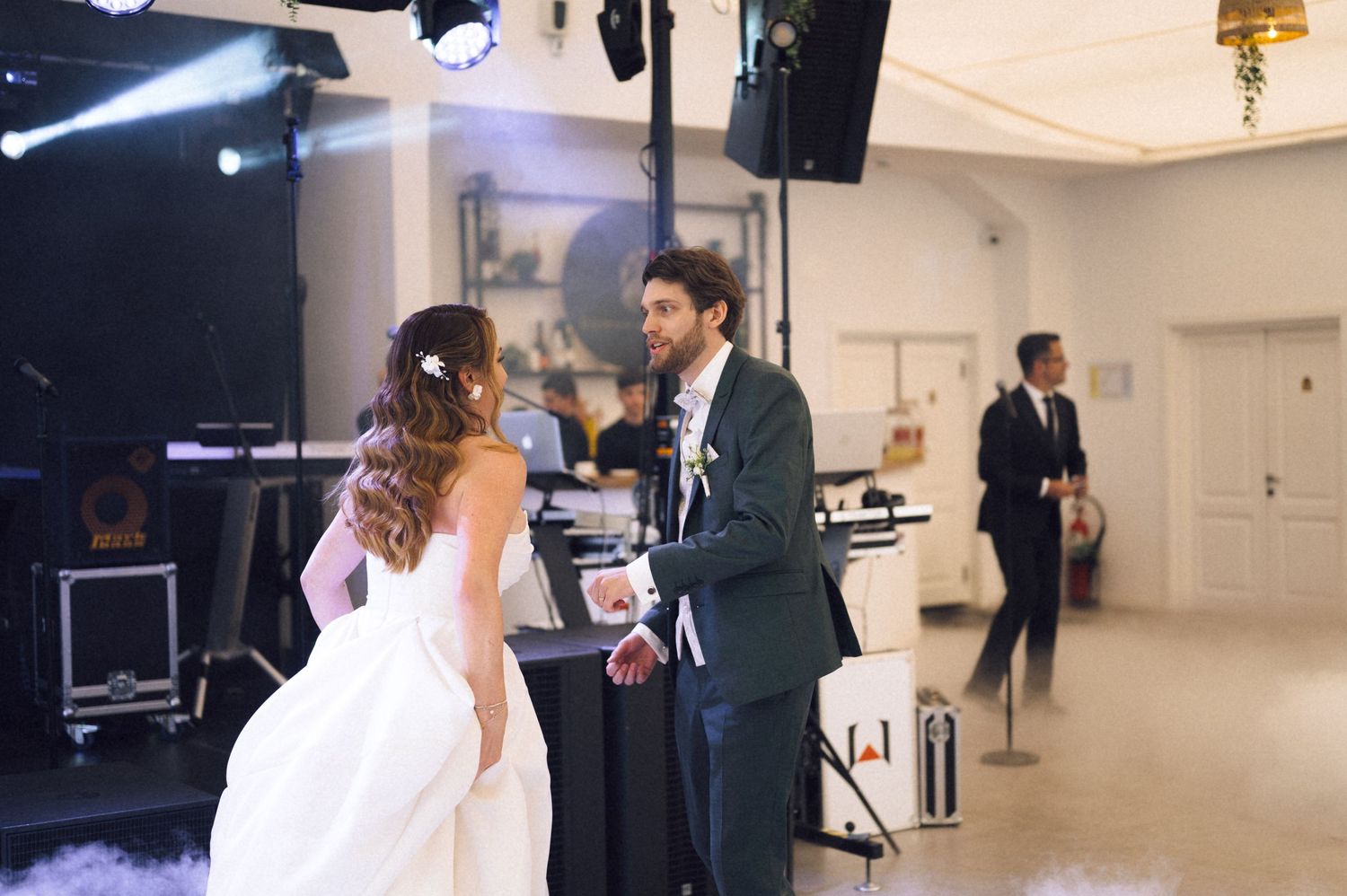 Bride and groom share first dance at elegant wedding reception with stage lighting and band equipment.