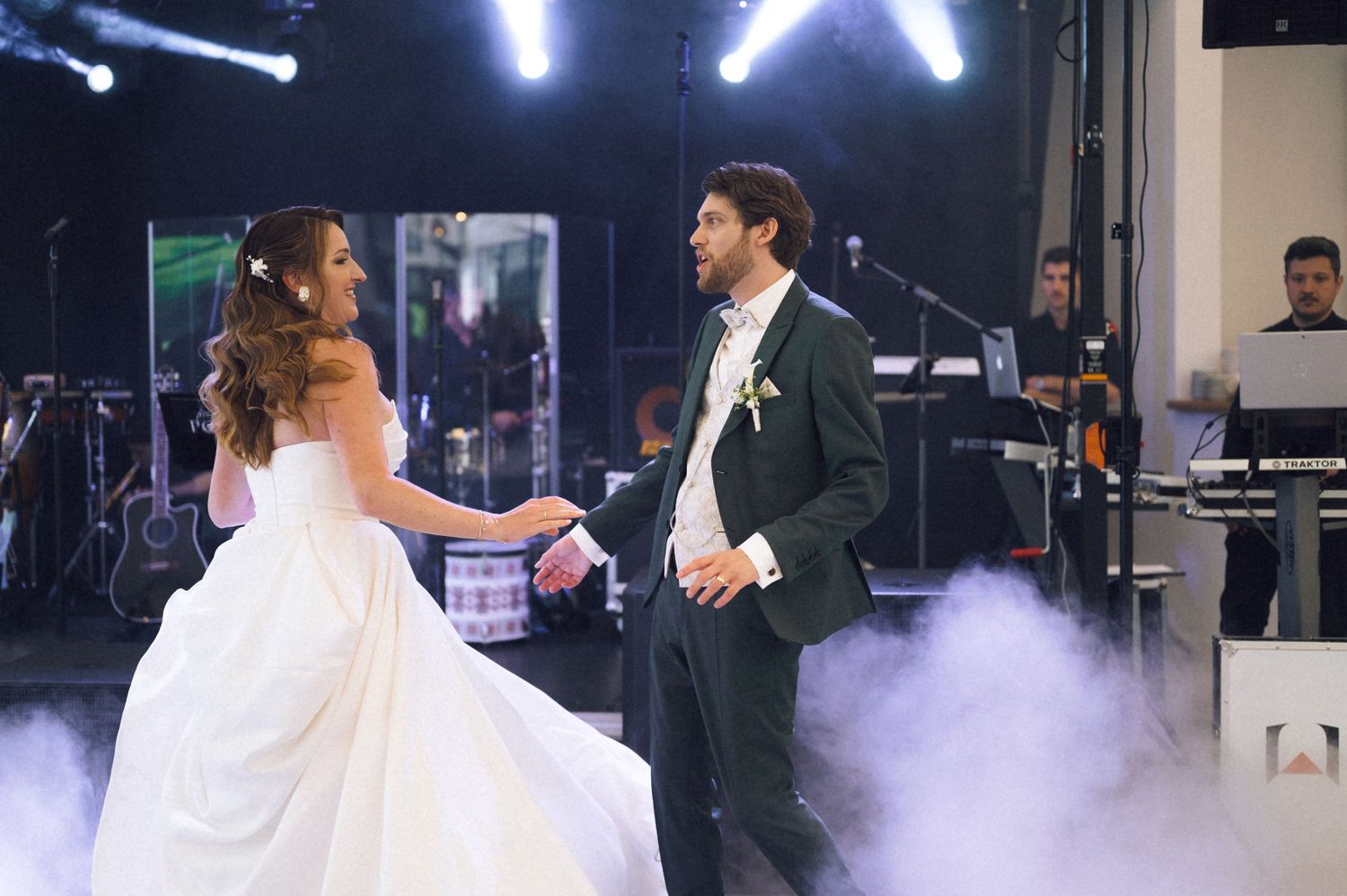 Bride and groom sharing their first dance on a foggy wedding reception stage with a live band performing behind them.