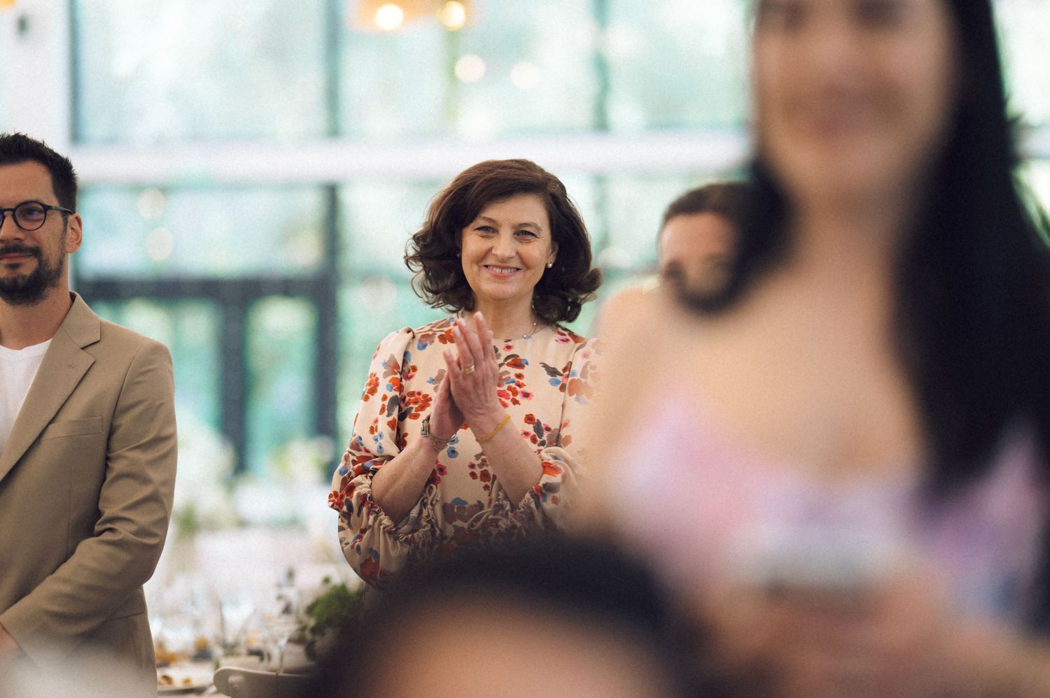 Woman in floral dress clapping and smiling at an elegant indoor wedding reception event.