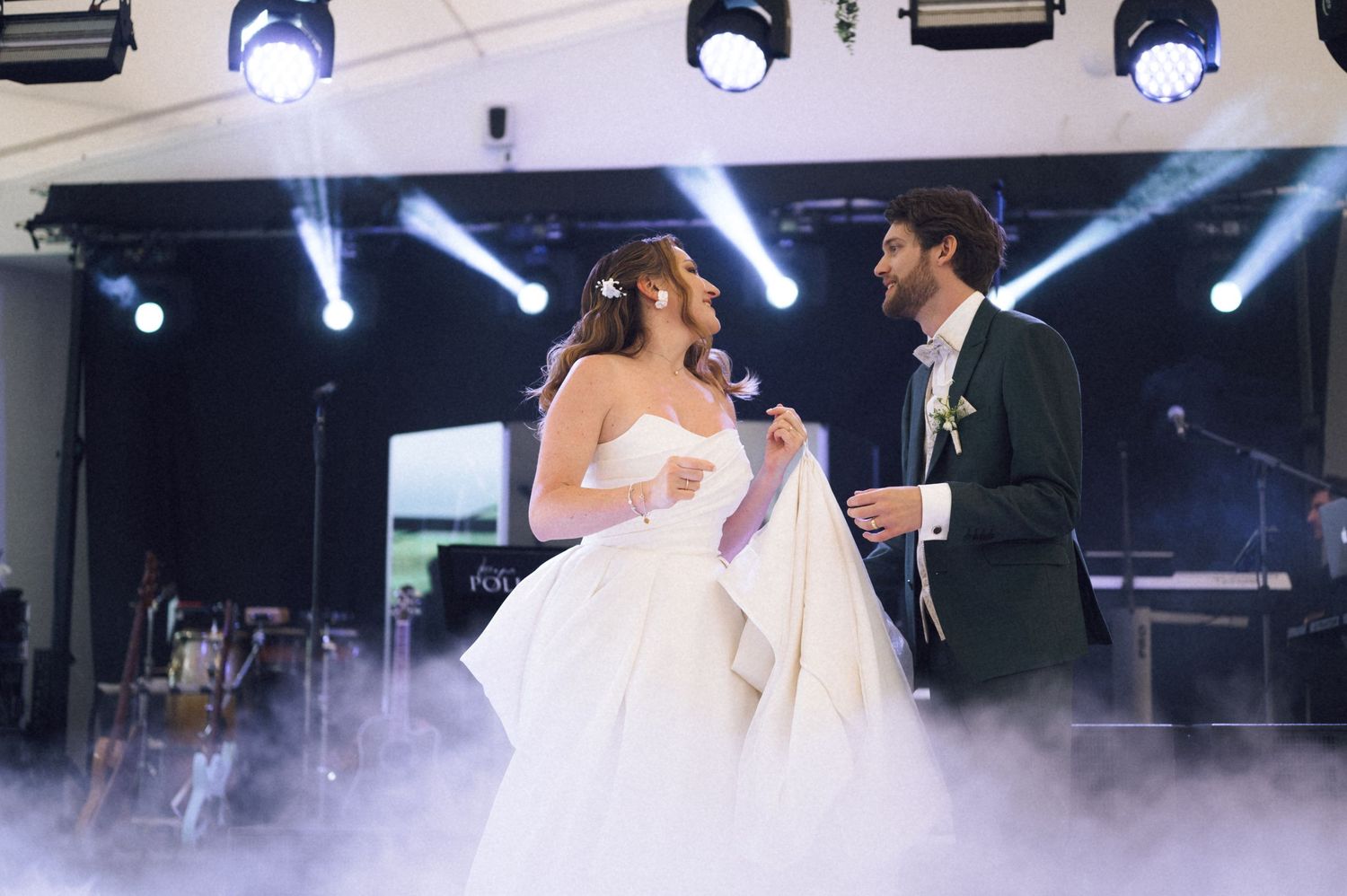 Bride and groom share their first dance on a foggy stage with dramatic lighting at their wedding reception.