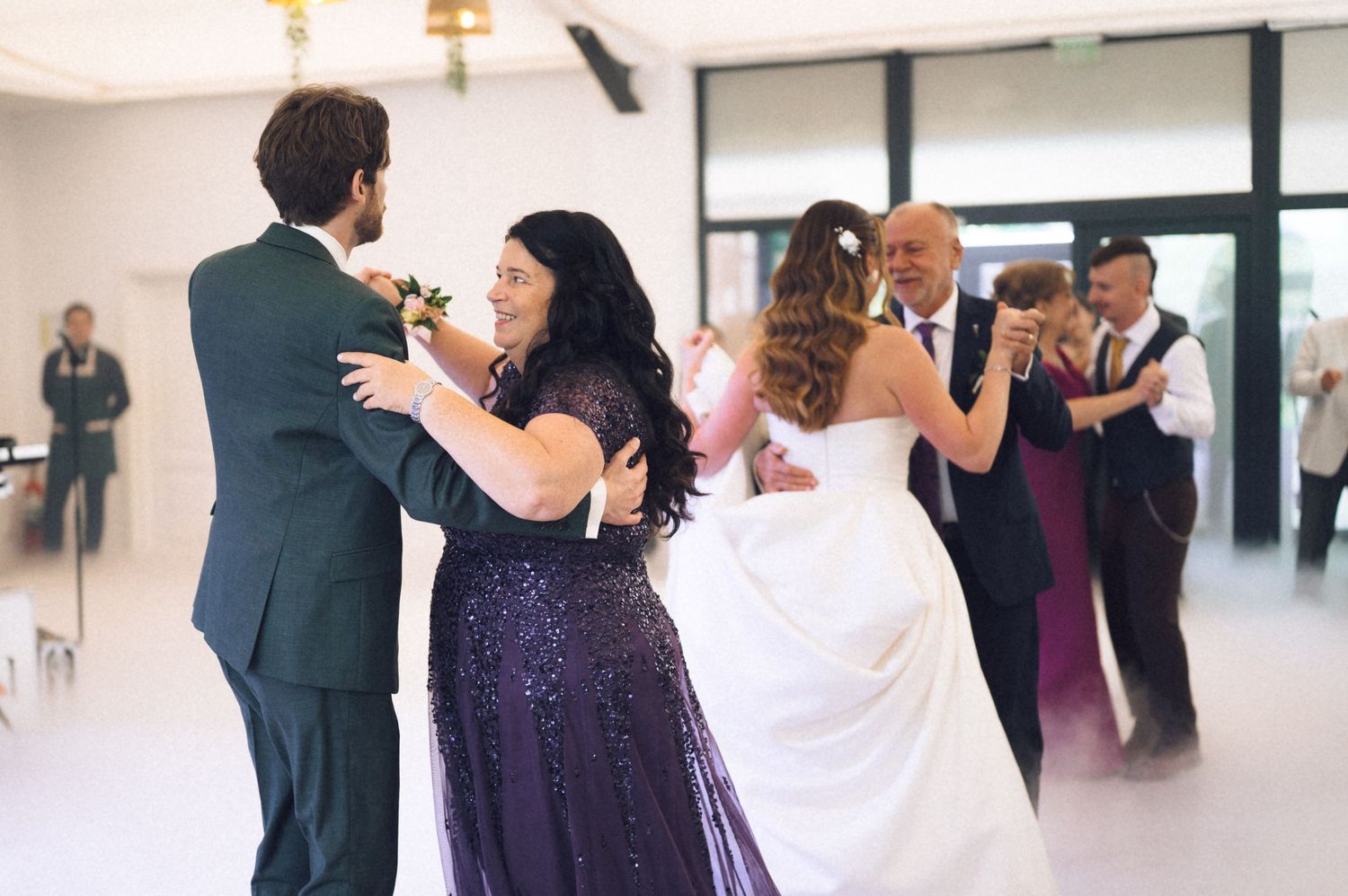 Wedding guests join the bride and groom on the dance floor during a joyful reception celebration.