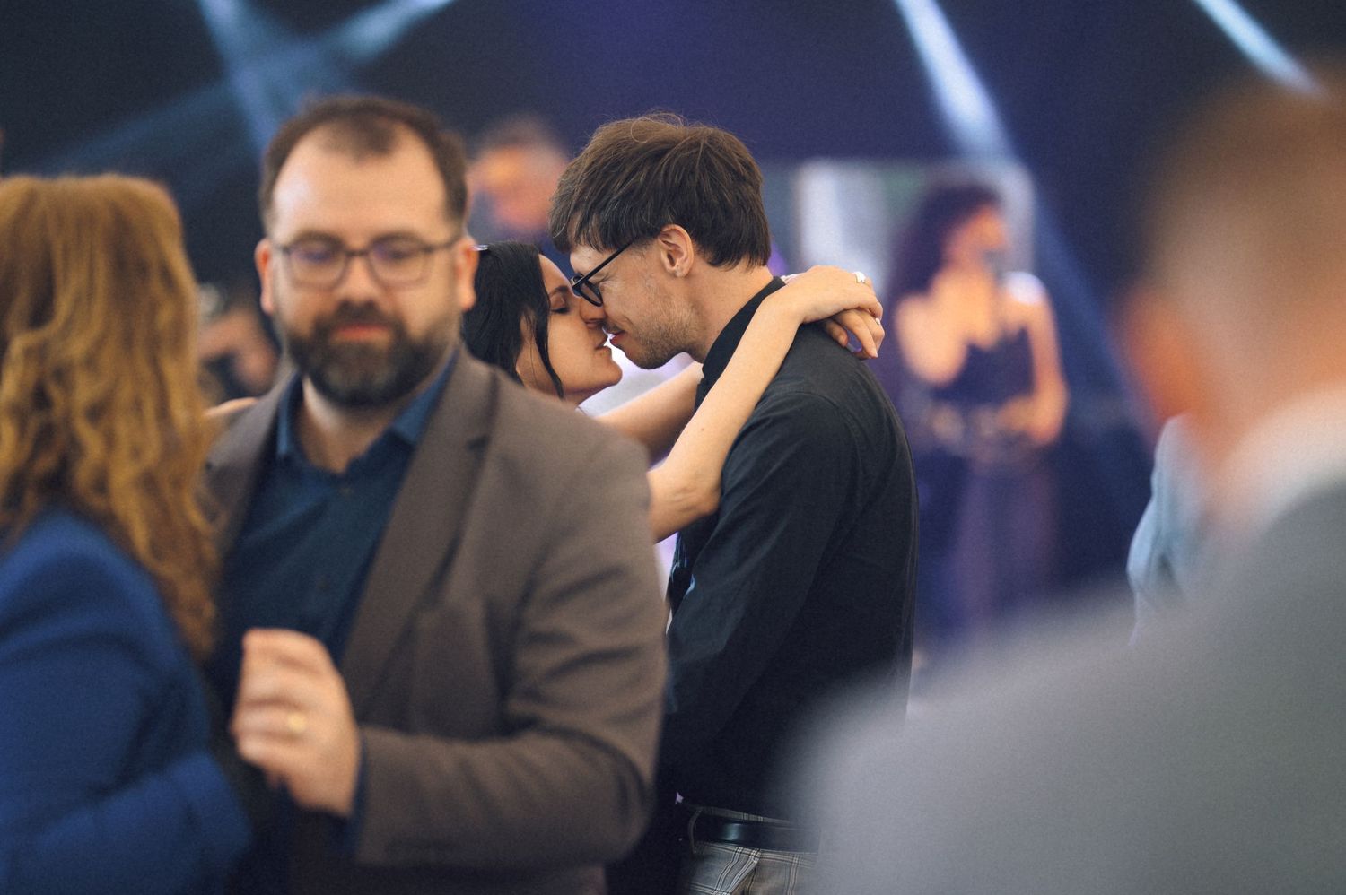 Couples dancing closely at a formal evening event, with guests in elegant attire in a softly lit venue.
