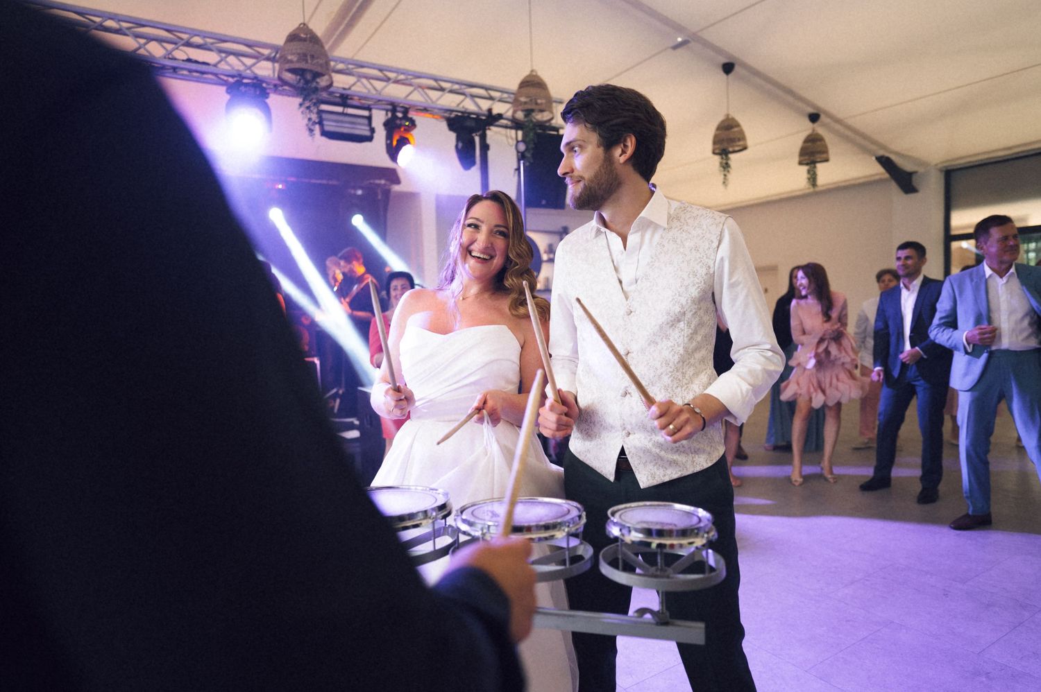 Couple joyfully playing drums with glowing drumsticks at a lively wedding reception party.