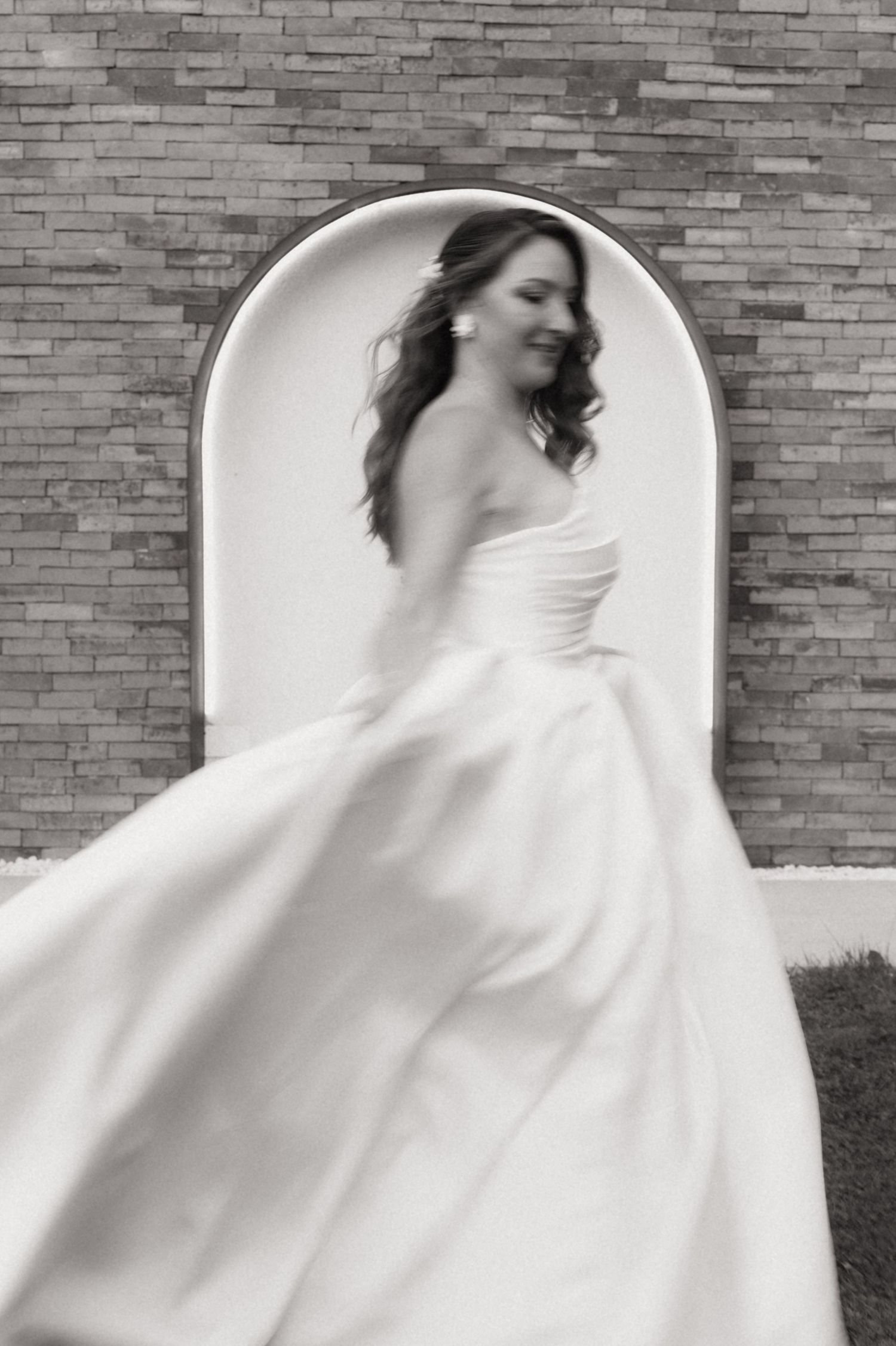 Black and white photo of a bride in a flowing strapless gown twirling before an arched doorway.