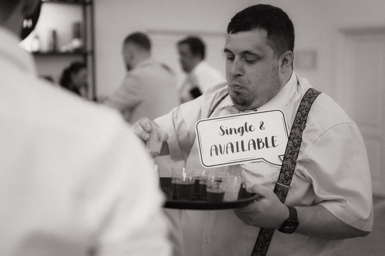 Man in white shirt holds tray with Single and Available sign at a wedding reception event.