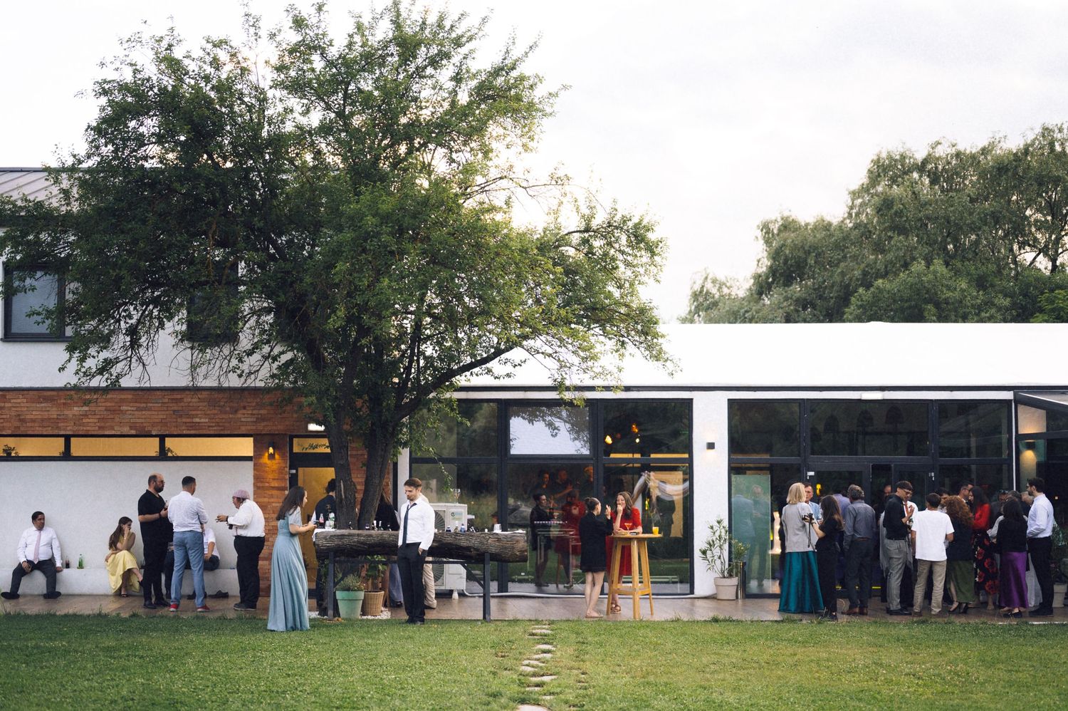 Guests mingling on a lawn outside a modern glass building during an outdoor evening social event.