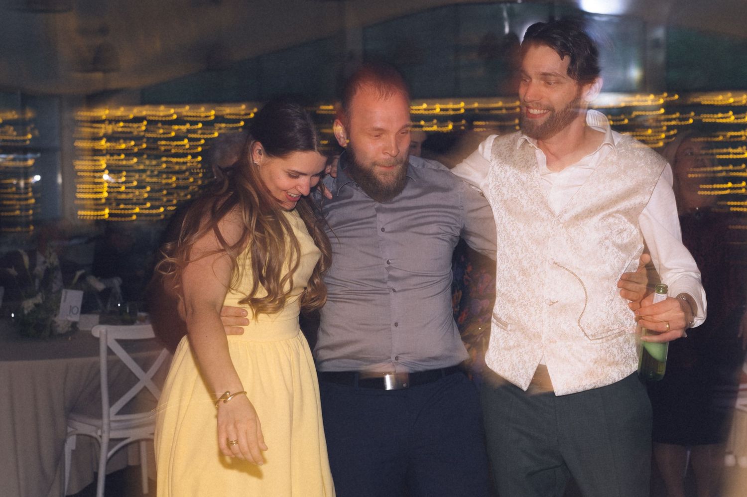 Three friends dancing and celebrating together at an indoor wedding reception party.