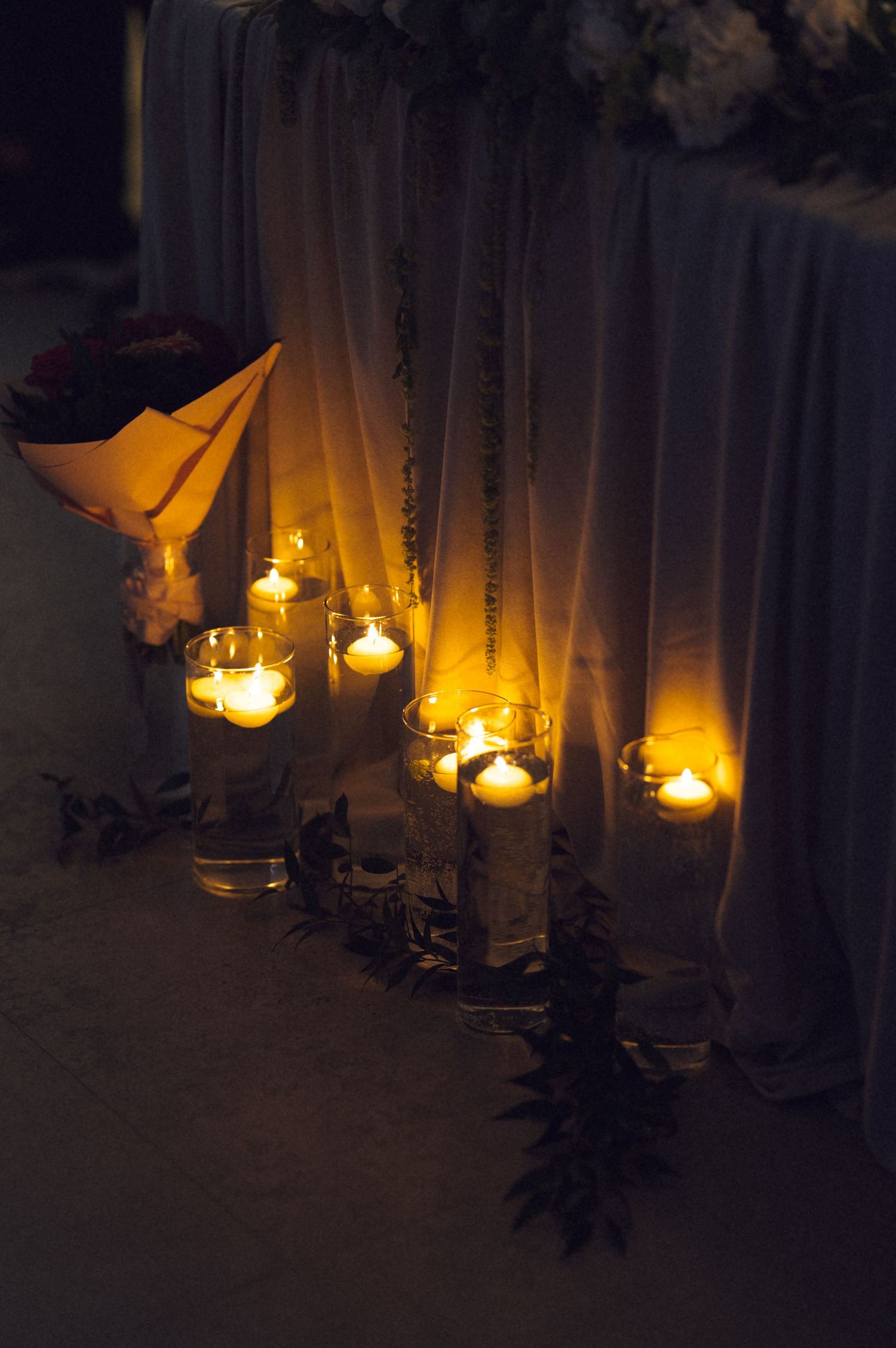 Glowing candles in glass holders arranged along draped white fabric at an elegant evening wedding reception.