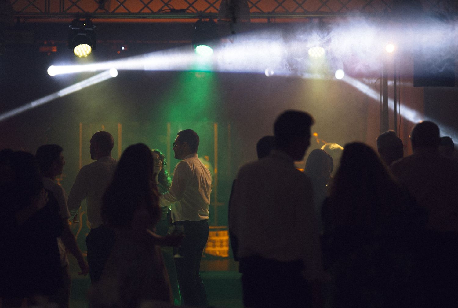 People dancing at a nightclub party with colorful stage lights and smoke effects in a dark venue.