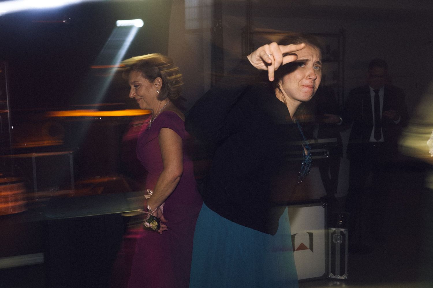 Two women dancing at a formal event, one in a purple dress and one in a blue skirt, under dramatic lighting.
