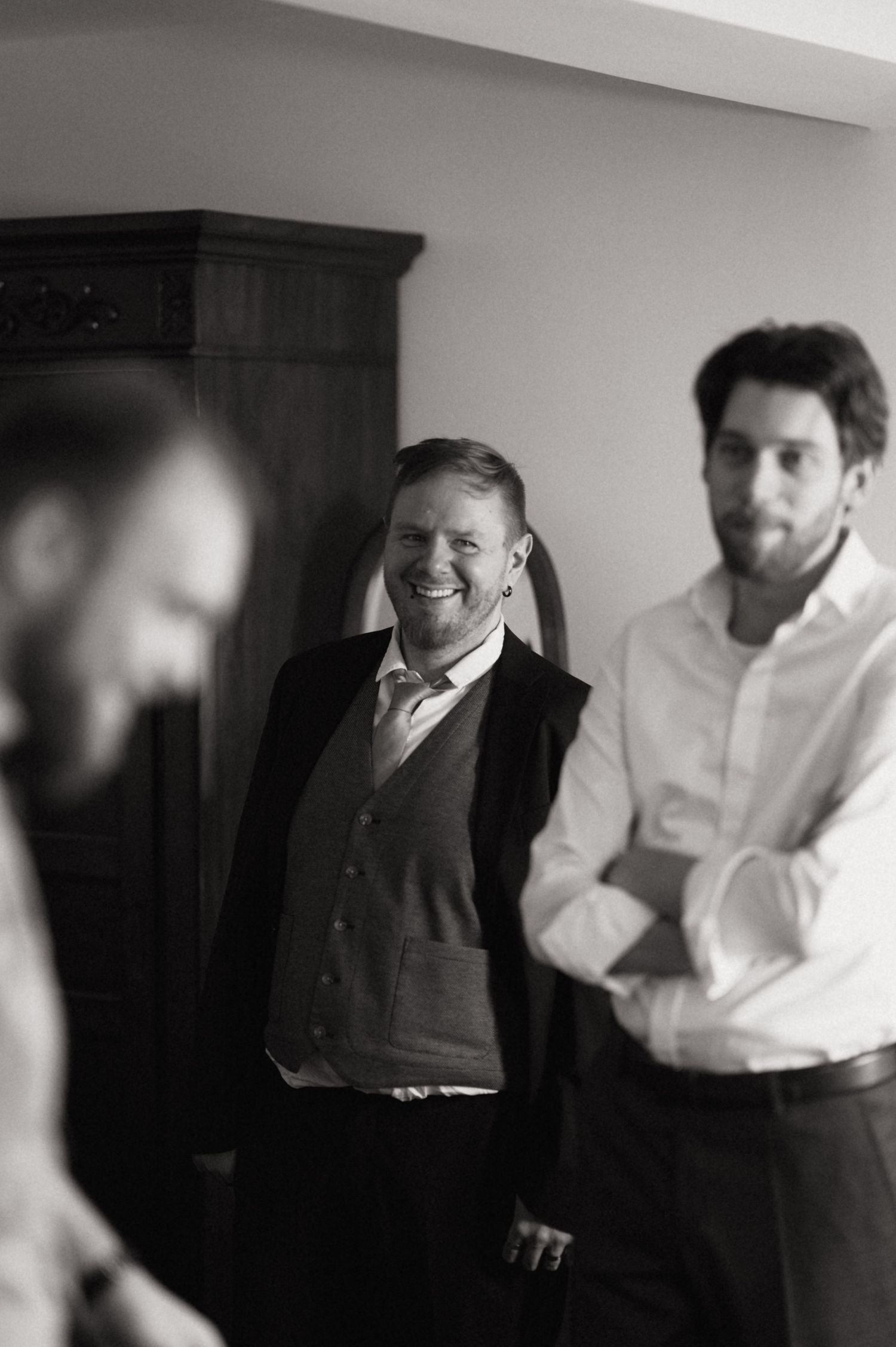 Black and white photo of three men smiling and conversing, dressed in formal attire, likely at a wedding event.