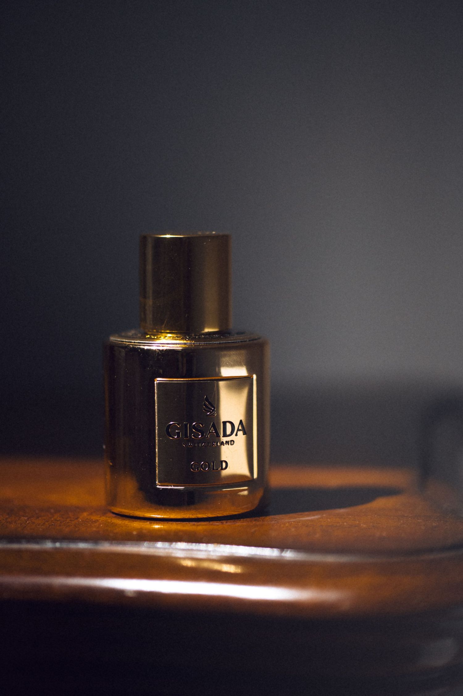 Gisada luxury gold perfume bottle displayed on a wooden surface against a dark background.