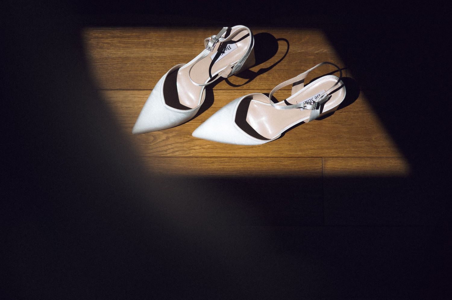 Elegant white and black pointed-toe slingback heels resting on hardwood floor in dramatic spotlight.