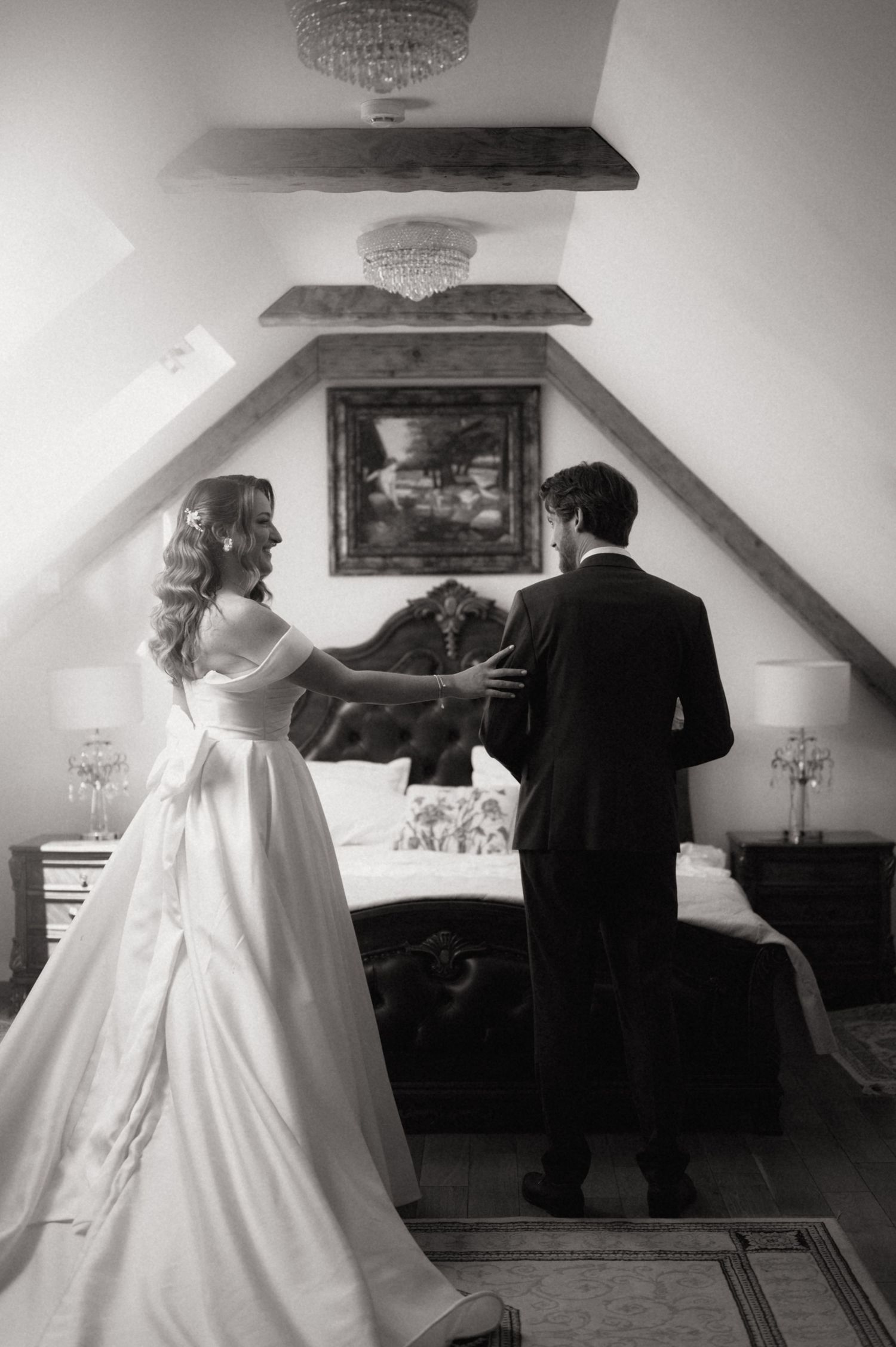 Black and white photo of a bride and groom sharing a tender moment in an elegant attic bedroom.
