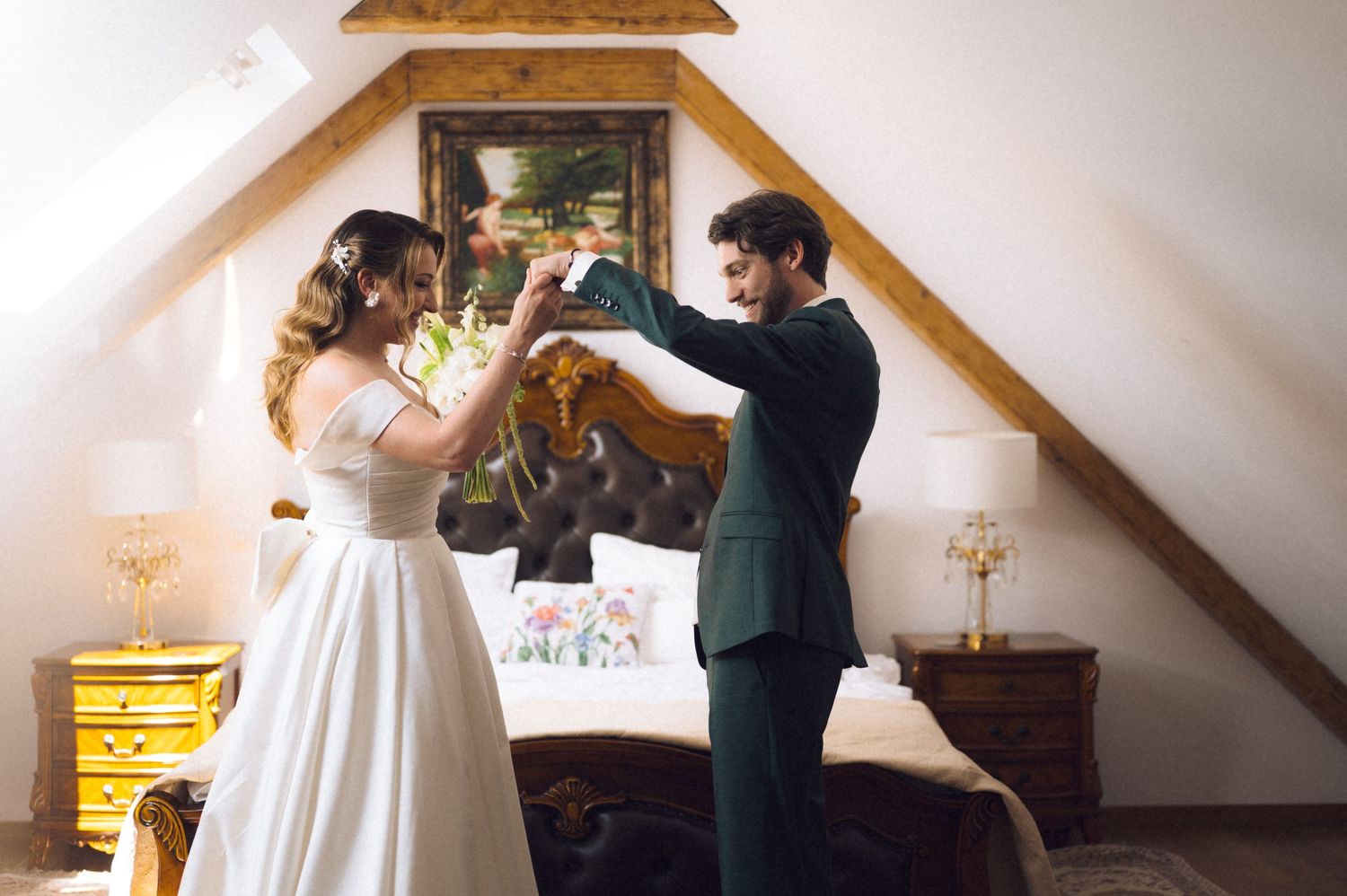 Bride and groom dancing together in a charming attic bedroom with wooden beams during their wedding celebration.
