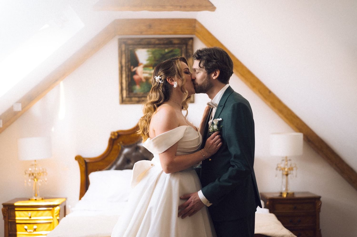 Bride and groom sharing a romantic kiss in a cozy attic bedroom with wooden beams on their wedding day.
