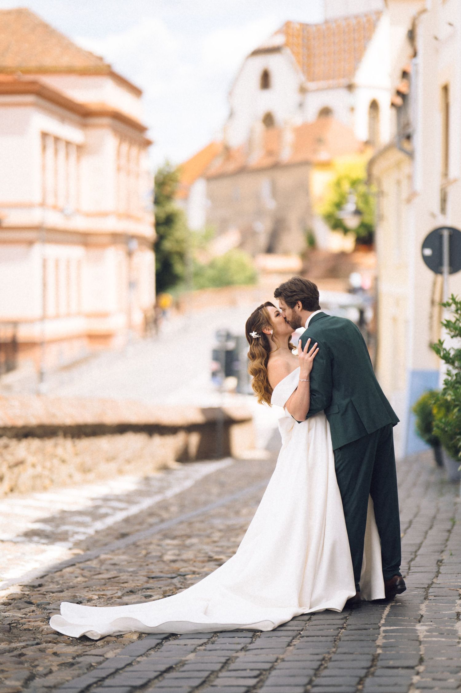 A bride and groom share a romantic kiss on a cobblestone street in a charming European town.