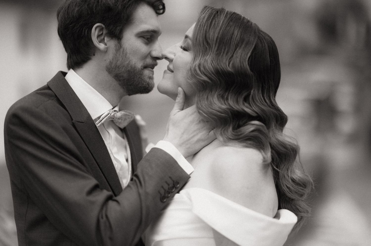 Black and white wedding photo of bride and groom sharing a romantic moment, almost kissing outdoors.