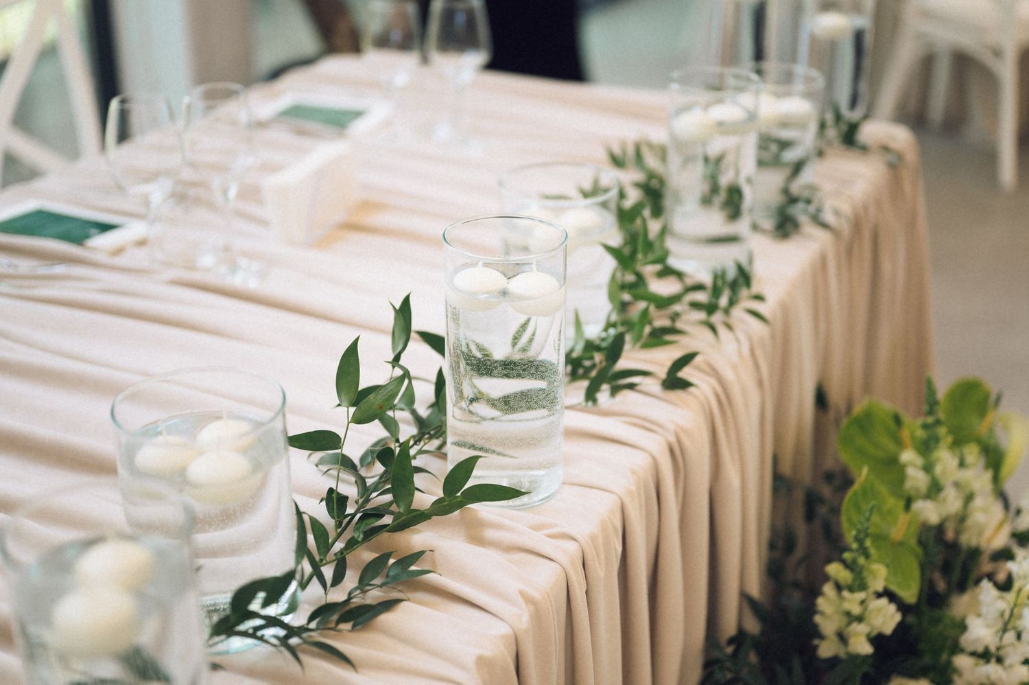 Elegant wedding head table with blush draping, floating candles, and lush greenery garland centerpiece.