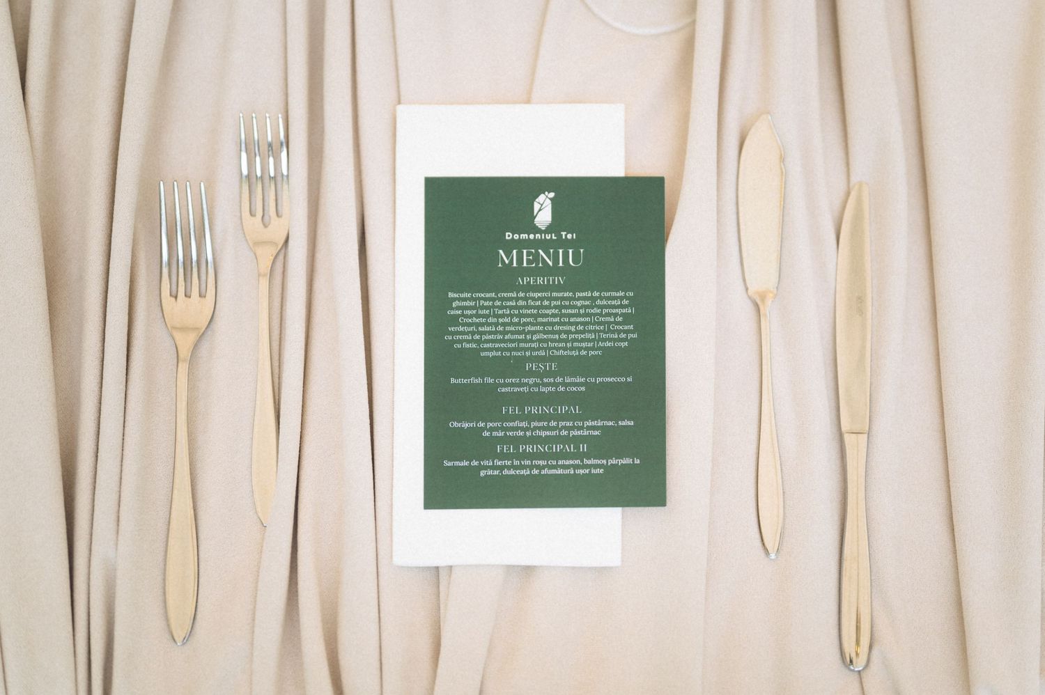 Wedding menu card with green design displayed between wooden forks and knife on beige linen.