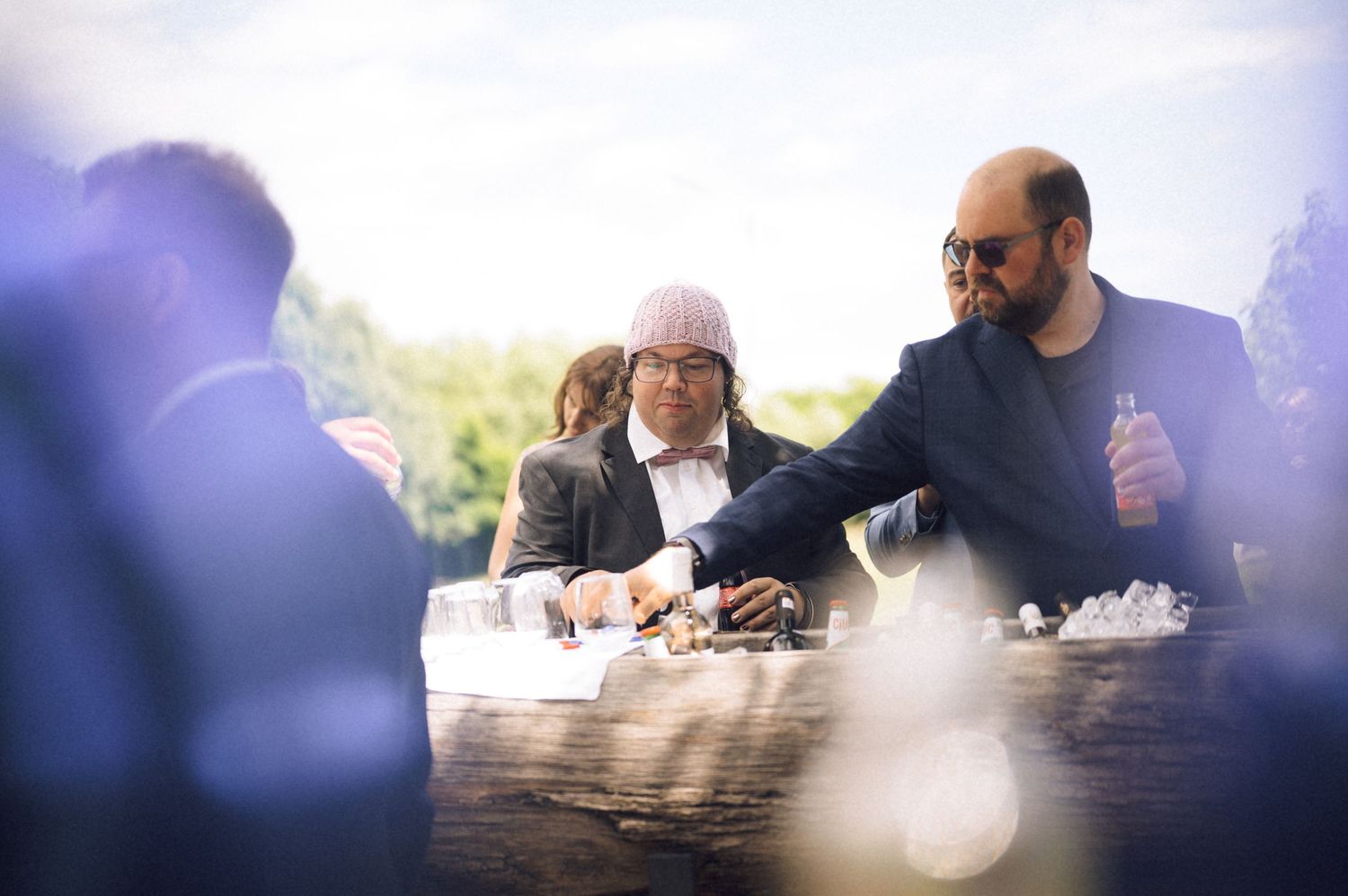Two men in formal attire enjoying oysters outdoors at an elegant social gathering on a sunny day.