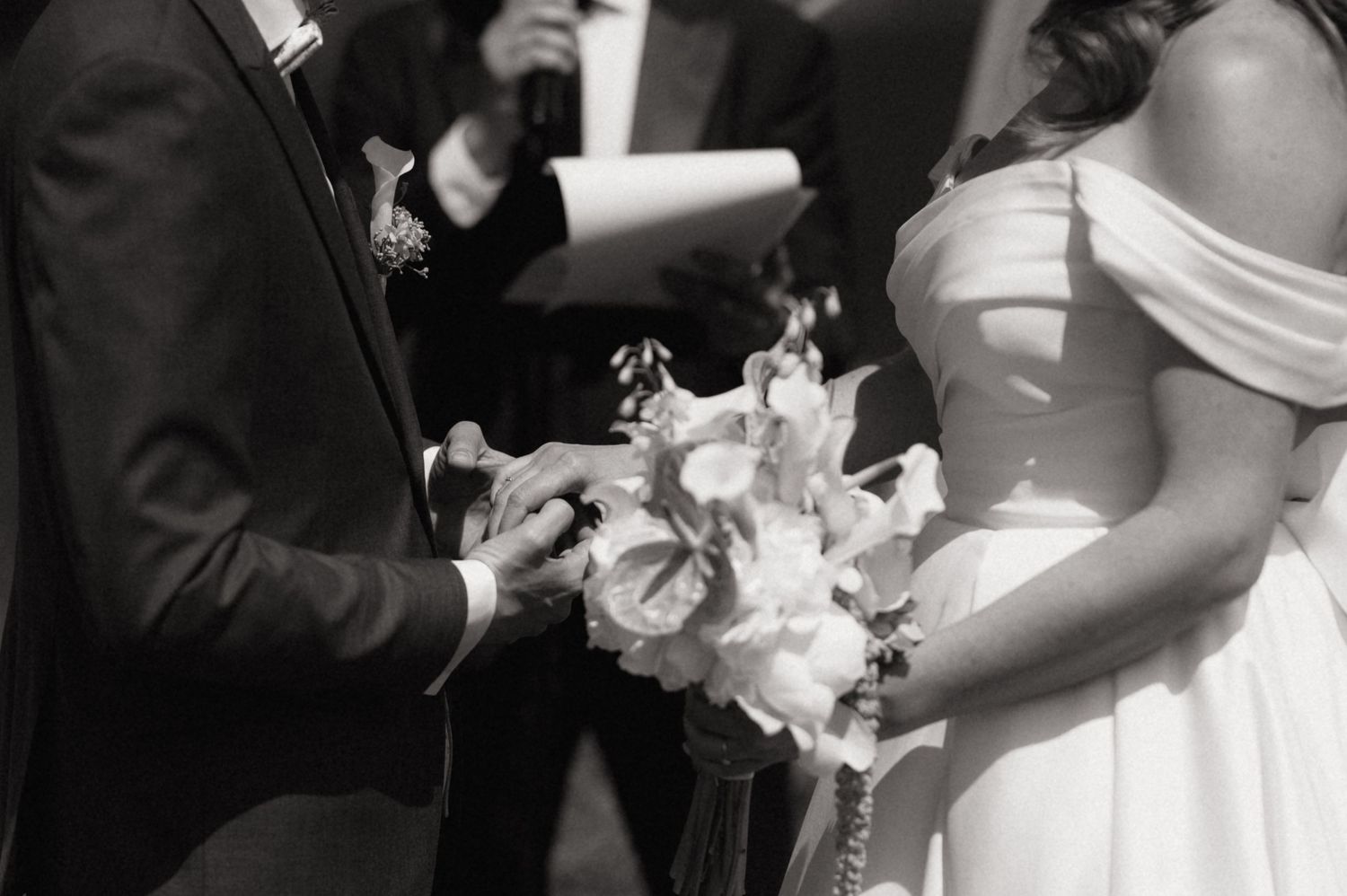 Black and white wedding ceremony photo of bride and groom holding hands while exchanging vows.