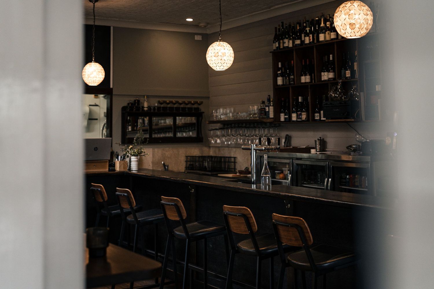 Dimly lit bar interior with pendant lights, bar stools, and shelves lined with wine bottles.

Surly Goat