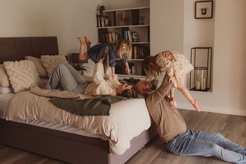 Playful family moment with children tumbling over parents on a bed in a bright bedroom.