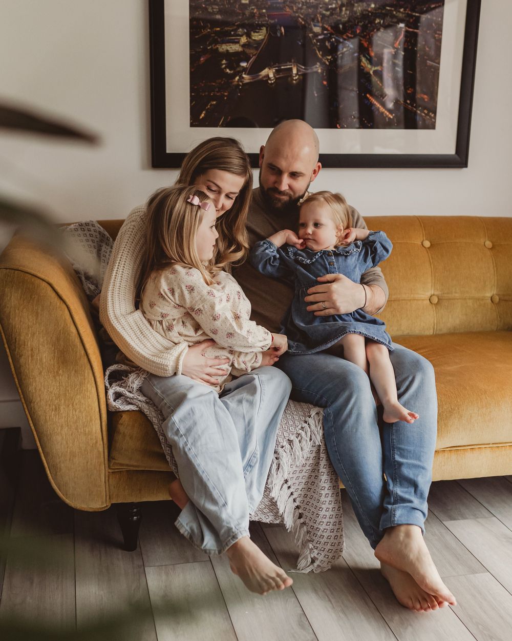 Young family of four sharing a tender moment together on a mustard yellow sofa at home.